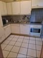 white tiled floor, white cabinets, black tiled wall, white sink, dishwasher, microwave, oven, countertop, silver appliances