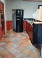Modern kitchen with tiled floor, black refrigerator, red cabinets, white walls, a sink with faucet, a gas stove, and a fan on the ceiling