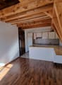Open kitchen with wooden beams, white cabinets, wooden countertop, white walls, wooden floor