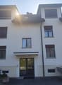 white 2 story building, multiple windows, sloped roof, paved entrance