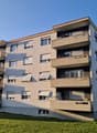 5-story apartment building, concrete balconies, flat roof, multiple windows, outdoor parking area