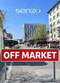 An empty city street with buildings on both sides, buses parked in the street, motorcycles parked in front of stores, an OFF MARKET sign, trees, and a person.