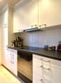 Modern kitchen with white cabinets, black countertop, built-in oven and stovetop, dishwasher, and various kitchen appliances and utensils