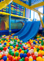 Colorful indoor playground with a blue slide, yellow climbing structures, and a ball pit filled with multicolored plastic balls.