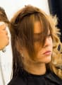 A woman with long blonde hair is getting her hair dried by a hair stylist using a hair dryer.