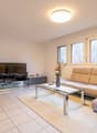 white tiles, beige sofa, glass coffee table, flat screen TV, cabinet, flowers, round lamp