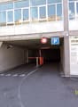The image shows the entrance to an underground parking garage. The entrance is marked with a parking sign and has a height limit of 2 meters. The garage appears to be located in a commercial or office building, with large glass windows on the upper floors
