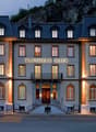 A multi-story hotel building with a traditional European architectural style, featuring stone walls, balconies, and large windows. The building is illuminated at night, creating a warm and inviting atmosphere. The name 'Klingele Haus' is prominently displ