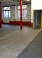 Empty room with red pillars, white walls, windows, radiator, open door, and a ladder.