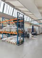 Large industrial warehouse with high ceilings, storage racks, and various materials and equipment stored on the premises. The space appears to be used for storage and distribution of goods.