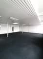 Large open office space with white walls, gray ceiling panels, and black carpeted floor. The room appears to be empty and ready for use.