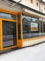 Exterior of a commercial building with glass windows, double-door entrance, signage, and orange frames. Snow on the ground and street.