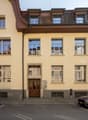 Four story building, double doors, many windows, parking space, gray color, brick facade