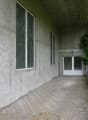 Concrete building with two large windows, brick pathway, white entrance door, and lamp on the right
