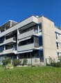 multi-storey building, concrete facade, balconies on upper floors, green fencing surrounding