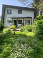 white house, flat roof, glass windows, covered entrance, garden with flowers, lawn, trees, bushes