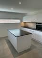Modern kitchen with island, white cabinets, black countertops, built-in oven and microwave, sink with faucet, and tiled flooring.