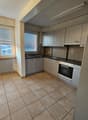 Kitchen with tiled flooring, a sink with faucet, a black countertop, built-in appliances including an oven and a dishwasher, white cabinets, and windows with blinds.