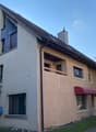 2 story house, beige exterior, brown roof, red awnings, balcony, windows, chimney