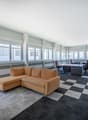 Large office space with a corner sofa, desk, and office chairs, equipped with white radiators and large windows.