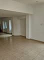 The image shows a large open room with a tiled floor. The walls are painted in a neutral color and there is a window overlooking what appears to be a garden or outdoor area. The room has a simple, minimalist design with no visible furniture or decor.