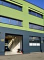 Industrial-style building, green exterior, multiple glass windows, car in the garage