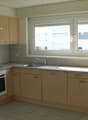 Spacious kitchen with light wood cabinets, granite countertops, stainless steel appliances including a dishwasher, and large windows providing natural light.
