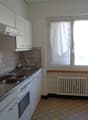 Compact kitchen with white cabinets, tiled backsplash, electric stove, dishwasher, and washing machine. The kitchen has a window providing natural light.