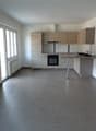 Empty kitchen with tiled floor, wooden cabinets, white walls, large windows, and a countertop with a sink and faucet.