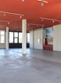 Empty room with red ceiling, white walls, concrete floor, large windows, and track lighting.