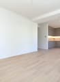 Empty room with wooden floor, white walls, kitchen with cabinets, microwave, and drawers, power outlets on the wall.