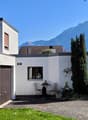 modern style house, white walls, brown roof, garage, large windows, surrounded by plants and trees, with a mountain view