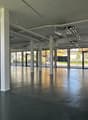 Empty industrial space with high ceilings, glass walls, concrete floor, and white columns, with natural light streaming in from the large windows.