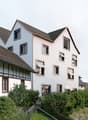 Multi-story building with a mix of traditional half-timbered and modern architectural styles, surrounded by lush greenery and vegetation.