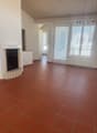 Spacious living room with terracotta tile flooring, white walls, and a fireplace. Large windows provide natural light and views. The room has an open layout with a high ceiling.