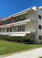 White apartment building, multiple balconies, well-maintained garden, paved walkway