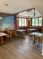 Cozy dining room with wooden tables and chairs, large windows, and a mural depicting a beach scene on the wall.