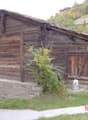 Old wooden cabin with a slanted roof, wooden walls, and a garage or storage area attached to the side.
