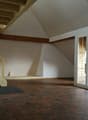 Empty room with wooden staircase, white walls, wooden beams, and red hexagonal tiles on the floor.
