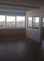 Large open space with tile flooring, multiple windows providing natural light, and a balcony or terrace visible through the windows.
