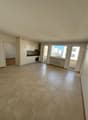 Empty room with tiled floor, white walls, kitchen area with sink, oven, and cabinets, sliding glass doors, and windows