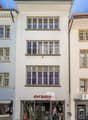 3 story building, glass windows, glass entrance with 'Orsay' text, street lamp, brick paved street
