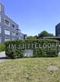 Modern apartment building with blue exterior, multiple windows, and a sign reading 'IM MITTELDORF'. The building is surrounded by greenery and has a driveway.