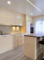 modern kitchen with white cabinets, wooden countertop, stainless steel sink, faucet, black bar stools, white appliances