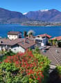 Scenic view of a lakeside town with colorful houses, palm trees, and mountains in the background. The houses have red tile roofs and are surrounded by lush greenery.