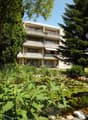 4-story apartment building with balconies, surrounded by lush greenery and a pond with water plants