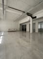 Large open office space with high ceilings, gray marble-like flooring, and a couch in the corner. The space appears to be empty and ready for use.