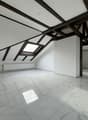 an attic room with a white tiled floor, dark wooden beams on the ceiling, skylights, a white pillar and a heater