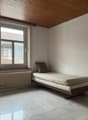 Empty room with a single bed, a window, a radiator, and a wooden ceiling.