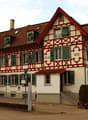 A traditional German half-timbered building with a red tiled roof, green shutters, and decorative wooden beams. The building appears to be a residential or commercial structure, with a sign indicating the year 1898.
